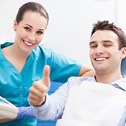 Female dentist and smiling man in dental chair giving thumbs up