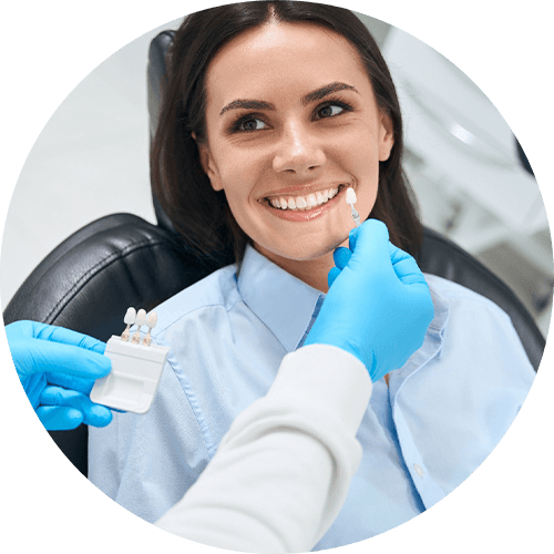 Woman in dental chair smiling at dentist holding shade guide to her teeth