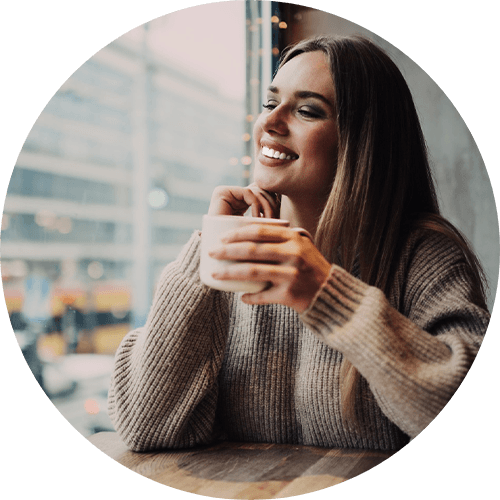 Woman in café smiling holding mug looking out the window